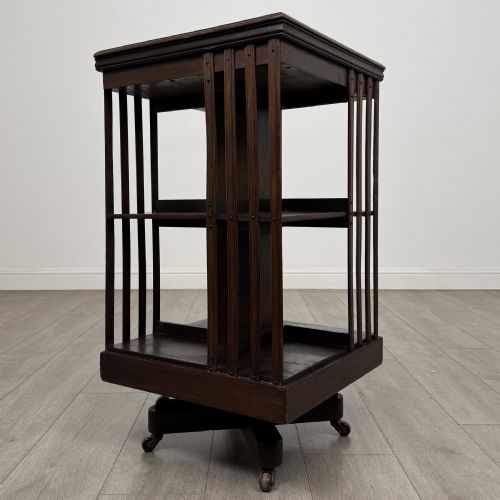 fig 3. A dark oak Edwardian revolving bookcase with vertical slatted sides, two shelf tiers, and a quadform base on castors.