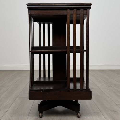 fig 4. A dark oak Edwardian revolving bookcase with vertical slatted sides, two shelf tiers, and a quadform base on castors.
