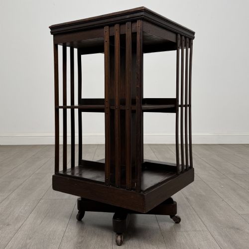 fig 5. A dark oak Edwardian revolving bookcase with vertical slatted sides, two shelf tiers, and a quadform base on castors.