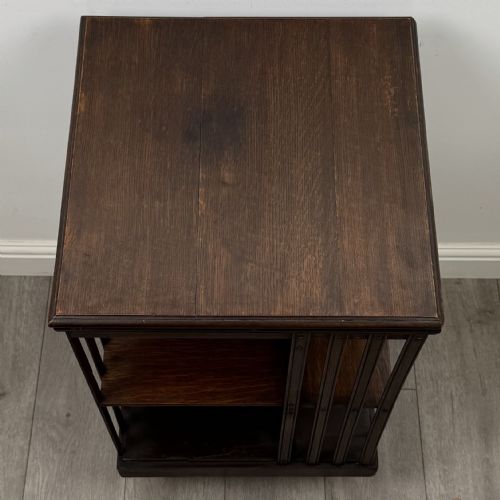 fig 6. A dark oak Edwardian revolving bookcase with vertical slatted sides, two shelf tiers, and a quadform base on castors.