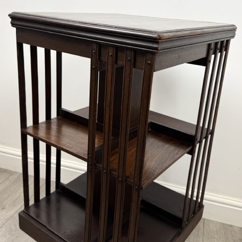 fig 7. A dark oak Edwardian revolving bookcase with vertical slatted sides, two shelf tiers, and a quadform base on castors.