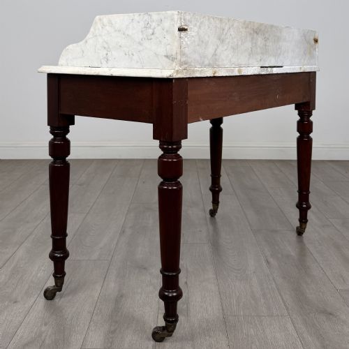 fig 3. A Victorian mahogany washstand featuring a white marble top with a raised splashback, two drawers with turned knobs, turned legs, and brass castors.