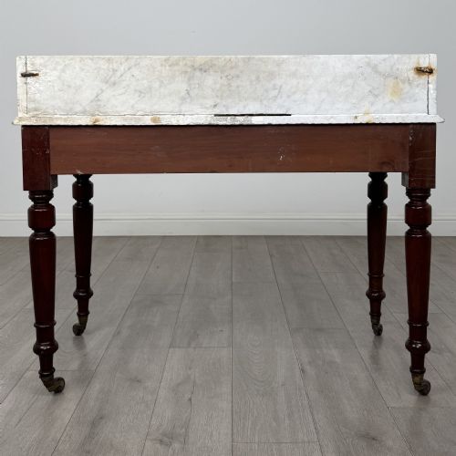 fig 4. A Victorian mahogany washstand featuring a white marble top with a raised splashback, two drawers with turned knobs, turned legs, and brass castors.