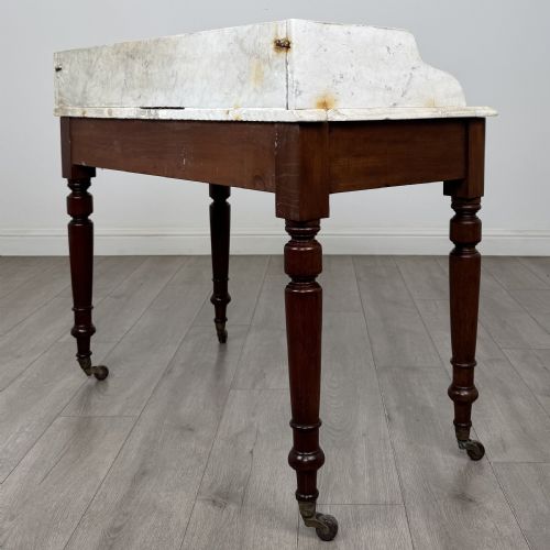fig 5. A Victorian mahogany washstand featuring a white marble top with a raised splashback, two drawers with turned knobs, turned legs, and brass castors.