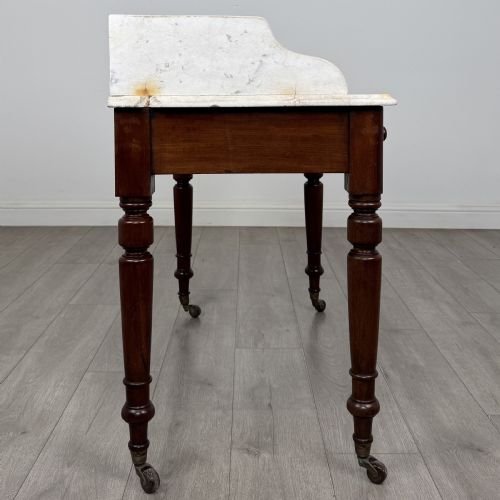 fig 6. A Victorian mahogany washstand featuring a white marble top with a raised splashback, two drawers with turned knobs, turned legs, and brass castors.