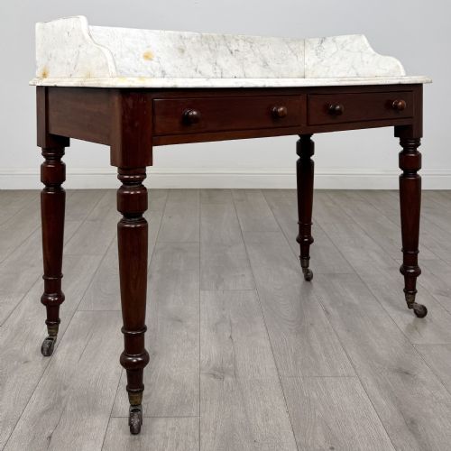 fig 7. A Victorian mahogany washstand featuring a white marble top with a raised splashback, two drawers with turned knobs, turned legs, and brass castors.
