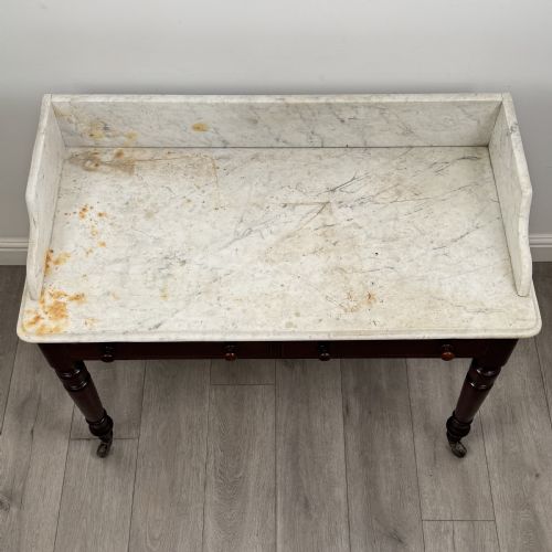 fig 8. A Victorian mahogany washstand featuring a white marble top with a raised splashback, two drawers with turned knobs, turned legs, and brass castors.
