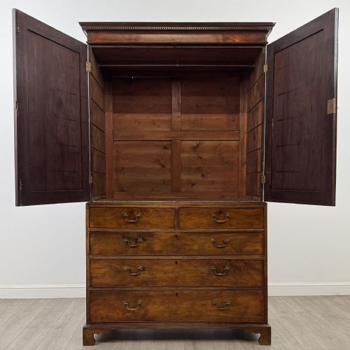 fig 1. An 18th-century Georgian mahogany linen press featuring flame mahogany door panels above four drawers with brass handles and bracket feet.