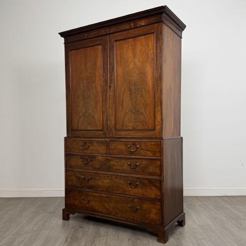 fig 2. An 18th-century Georgian mahogany linen press featuring flame mahogany door panels above four drawers with brass handles and bracket feet.