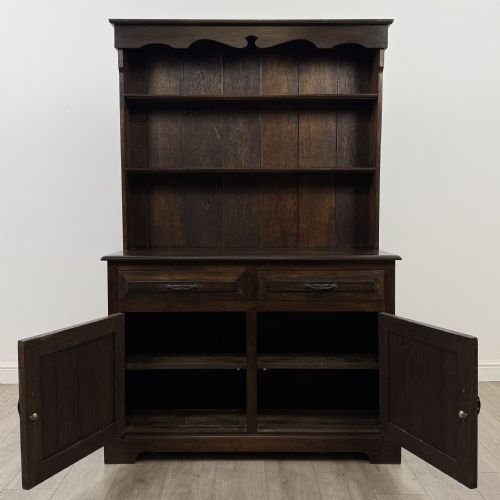 fig 1. A dark oak Welsh dresser featuring an upper plate rack with open shelves set above a two-drawer, two-door base cabinet.