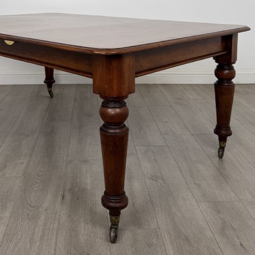 fig 3. A 19th-century Victorian mahogany dining table featuring turned legs fitted with brass castors and a rectangular top with rounded corners.
