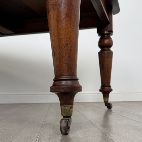 fig 4. A 19th-century Victorian mahogany dining table featuring turned legs fitted with brass castors and a rectangular top with rounded corners.