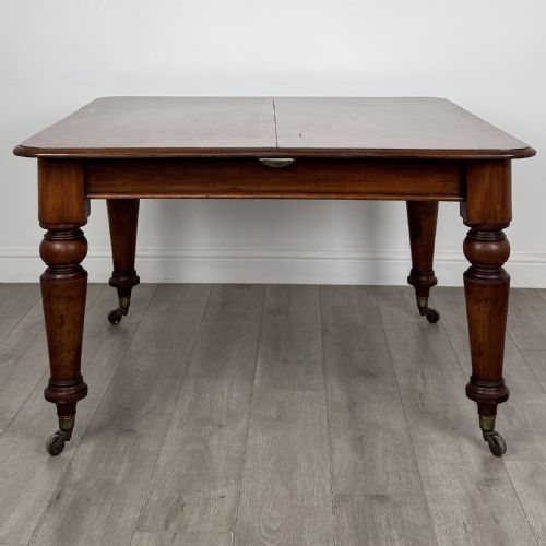 fig 7. A 19th-century Victorian mahogany dining table featuring turned legs fitted with brass castors and a rectangular top with rounded corners.