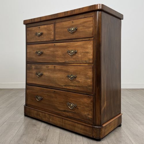 fig 1. An Edwardian walnut chest of drawers featuring two short drawers over three long drawers with ornate brass handles.