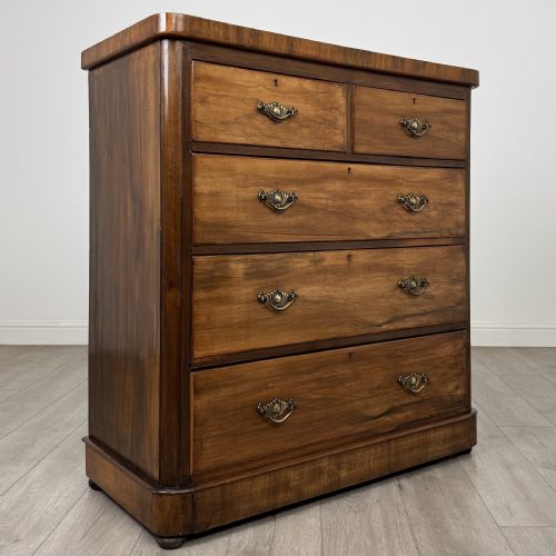 fig 7. An Edwardian walnut chest of drawers featuring two short drawers over three long drawers with ornate brass handles.