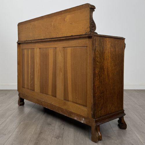 fig 6. An antique golden oak Art Deco sideboard featuring a carved gallery back, four central drawers, flanked cupboard doors with carved floral panels, and sculpted wooden handles.