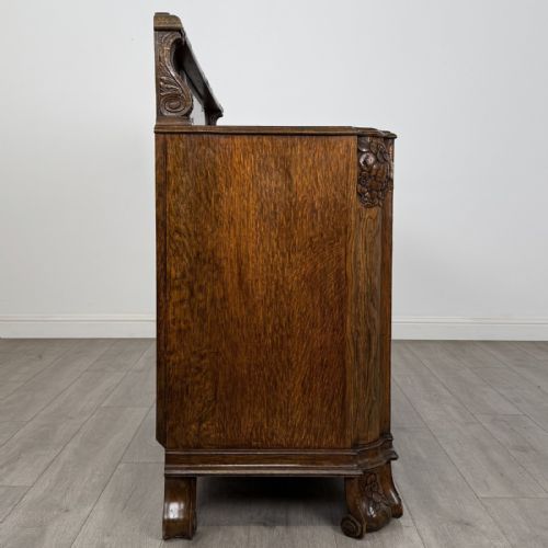 fig 7. An antique golden oak Art Deco sideboard featuring a carved gallery back, four central drawers, flanked cupboard doors with carved floral panels, and sculpted wooden handles.