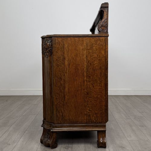 fig 3. An antique golden oak Art Deco sideboard featuring a carved gallery back, four central drawers, flanked cupboard doors with carved floral panels, and sculpted wooden handles.
