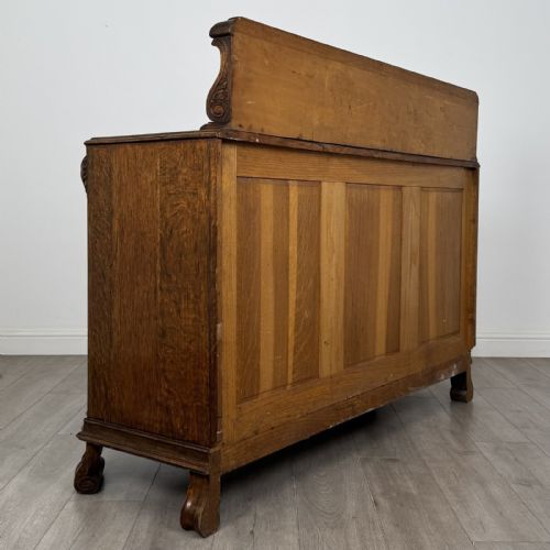 fig 4. An antique golden oak Art Deco sideboard featuring a carved gallery back, four central drawers, flanked cupboard doors with carved floral panels, and sculpted wooden handles.
