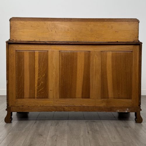 fig 5. An antique golden oak Art Deco sideboard featuring a carved gallery back, four central drawers, flanked cupboard doors with carved floral panels, and sculpted wooden handles.