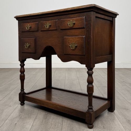 fig 1. A dark oak side table featuring five drawers with brass handles, turned front legs, an arched kneehole, and a lower tier shelf.