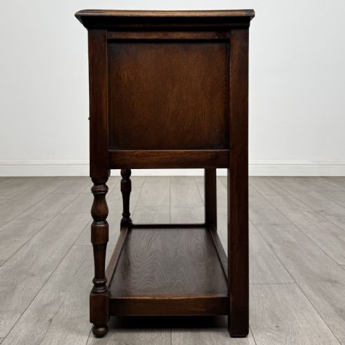 fig 2. A dark oak side table featuring five drawers with brass handles, turned front legs, an arched kneehole, and a lower tier shelf.