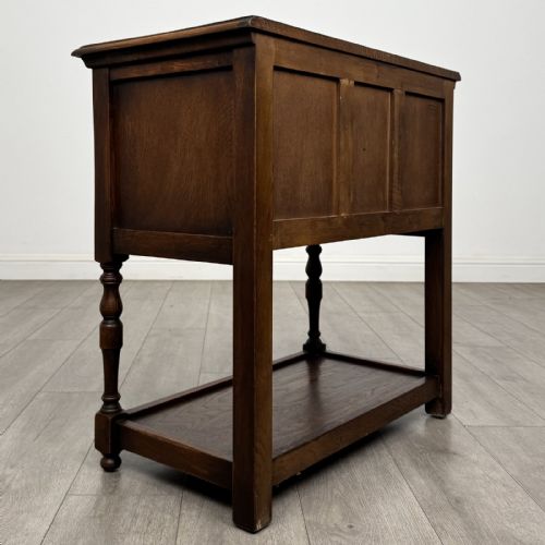 fig 3. A dark oak side table featuring five drawers with brass handles, turned front legs, an arched kneehole, and a lower tier shelf.