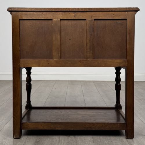 fig 4. A dark oak side table featuring five drawers with brass handles, turned front legs, an arched kneehole, and a lower tier shelf.