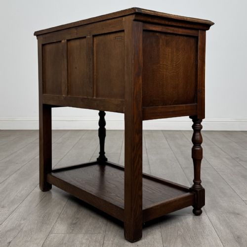 fig 5. A dark oak side table featuring five drawers with brass handles, turned front legs, an arched kneehole, and a lower tier shelf.