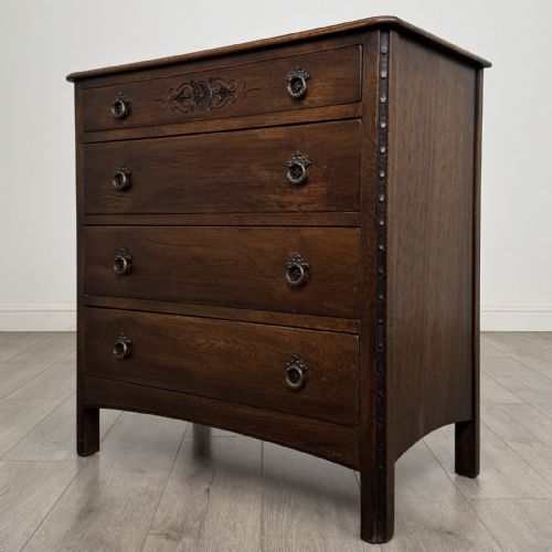 fig 1. A dark brown carved oak chest of drawers featuring four stacked drawers with drop ring handles and an incised rosette carving on the top drawer.