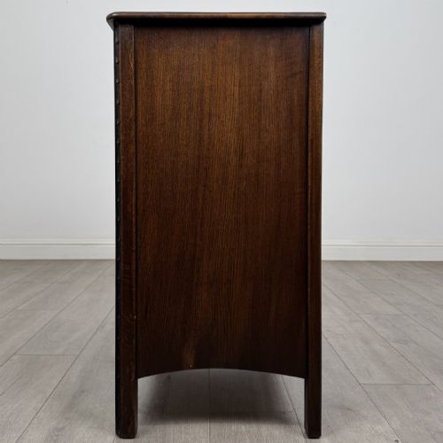 fig 2. A dark brown carved oak chest of drawers featuring four stacked drawers with drop ring handles and an incised rosette carving on the top drawer.