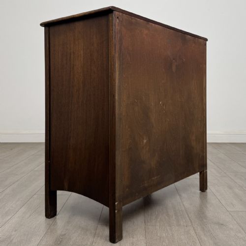 fig 3. A dark brown carved oak chest of drawers featuring four stacked drawers with drop ring handles and an incised rosette carving on the top drawer.