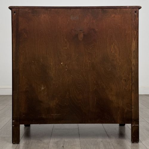fig 4. A dark brown carved oak chest of drawers featuring four stacked drawers with drop ring handles and an incised rosette carving on the top drawer.