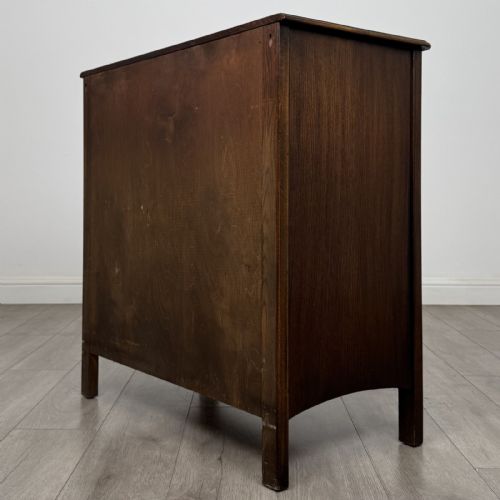 fig 5. A dark brown carved oak chest of drawers featuring four stacked drawers with drop ring handles and an incised rosette carving on the top drawer.