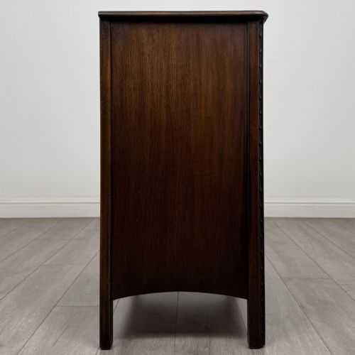 fig 6. A dark brown carved oak chest of drawers featuring four stacked drawers with drop ring handles and an incised rosette carving on the top drawer.