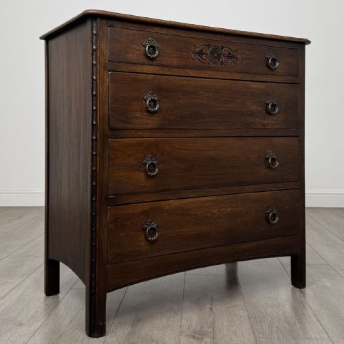 fig 7. A dark brown carved oak chest of drawers featuring four stacked drawers with drop ring handles and an incised rosette carving on the top drawer.