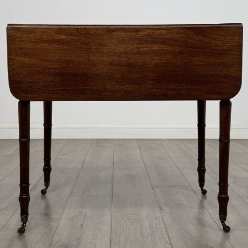 fig 1. An antique Regency style mahogany Pembroke side table featuring drop leaves, turned reeded legs, a single drawer with decorative inlay, and brass wheel castors.