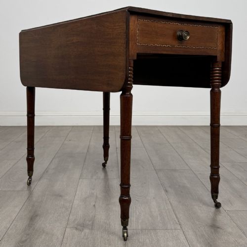 fig 2. An antique Regency style mahogany Pembroke side table featuring drop leaves, turned reeded legs, a single drawer with decorative inlay, and brass wheel castors.