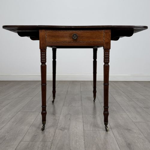 fig 3. An antique Regency style mahogany Pembroke side table featuring drop leaves, turned reeded legs, a single drawer with decorative inlay, and brass wheel castors.