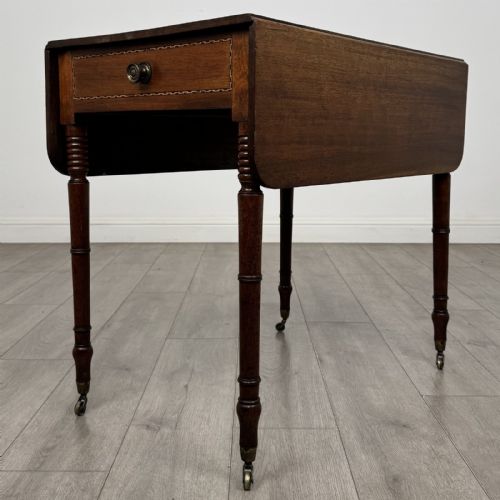 fig 4. An antique Regency style mahogany Pembroke side table featuring drop leaves, turned reeded legs, a single drawer with decorative inlay, and brass wheel castors.
