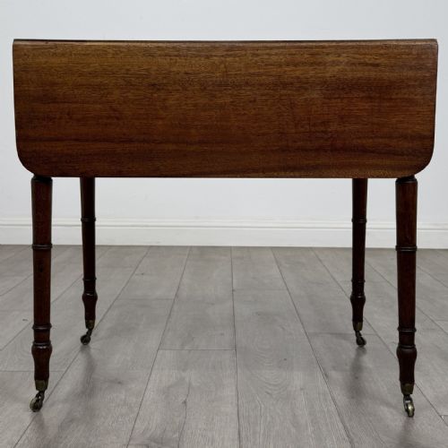 fig 5. An antique Regency style mahogany Pembroke side table featuring drop leaves, turned reeded legs, a single drawer with decorative inlay, and brass wheel castors.
