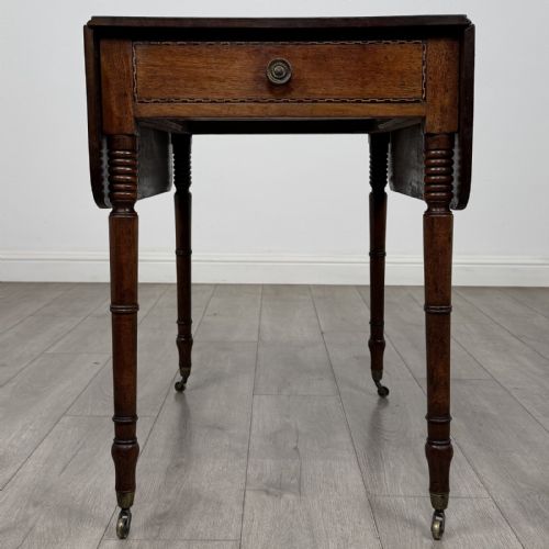 fig 7. An antique Regency style mahogany Pembroke side table featuring drop leaves, turned reeded legs, a single drawer with decorative inlay, and brass wheel castors.