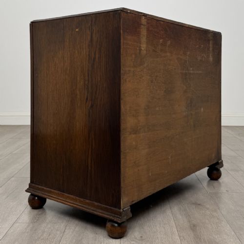 fig 3. A dark oak chest of three drawers featuring carved decorative detailing along the top edge, circular ring handles, and turned bun feet.