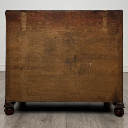fig 4. A dark oak chest of three drawers featuring carved decorative detailing along the top edge, circular ring handles, and turned bun feet.