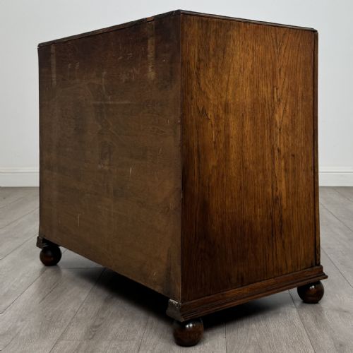 fig 5. A dark oak chest of three drawers featuring carved decorative detailing along the top edge, circular ring handles, and turned bun feet.