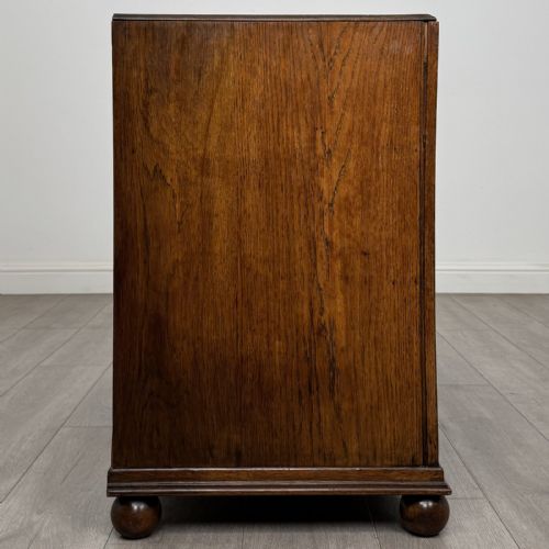 fig 6. A dark oak chest of three drawers featuring carved decorative detailing along the top edge, circular ring handles, and turned bun feet.