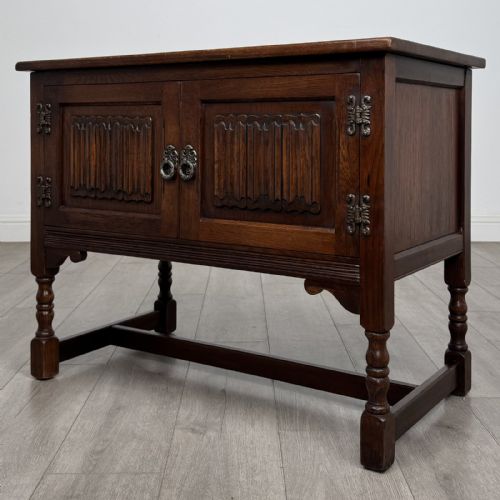 fig 3. A dark oak cupboard featuring two linenfold carved door panels, decorative metal hinges, ring pull handles, turned legs, and a lift top.