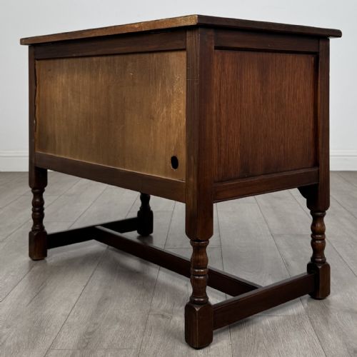 fig 7. A dark oak cupboard featuring two linenfold carved door panels, decorative metal hinges, ring pull handles, turned legs, and a lift top.
