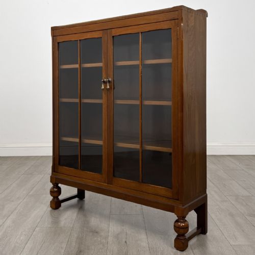 fig 2. A warm brown antique oak display cabinet featuring two glazed doors with wooden glazing bars and squat turned legs.