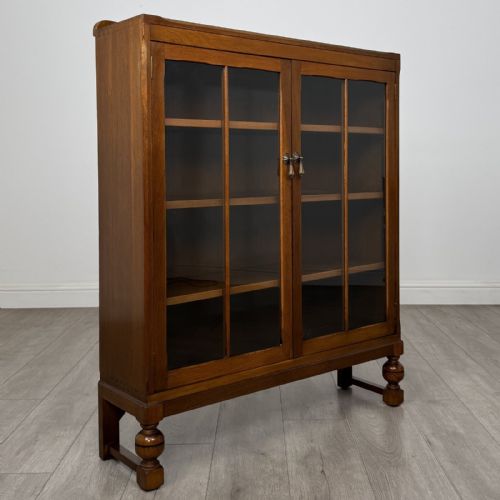 fig 8. A warm brown antique oak display cabinet featuring two glazed doors with wooden glazing bars and squat turned legs.